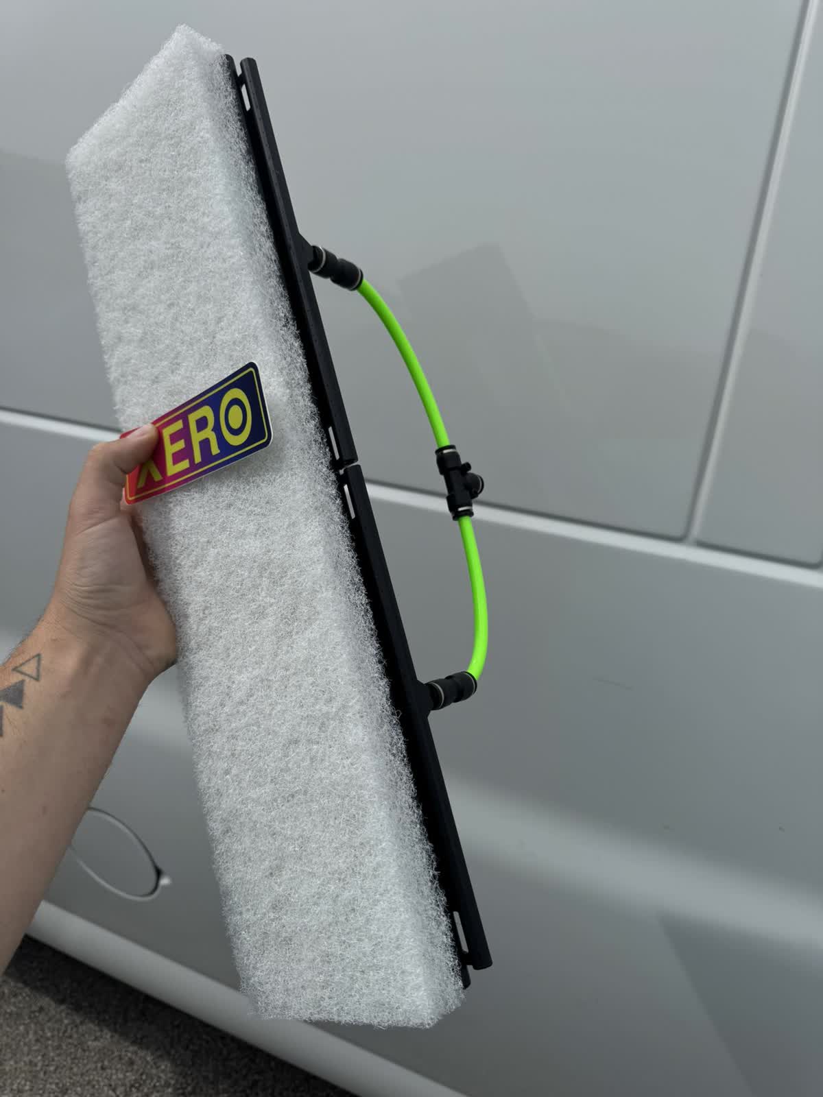 The actual tool we use: a soft scrub-pad head for a water-fed pole, with the neon-green deionized water feed line attached — no bristles stiff enough to scratch, no pressure