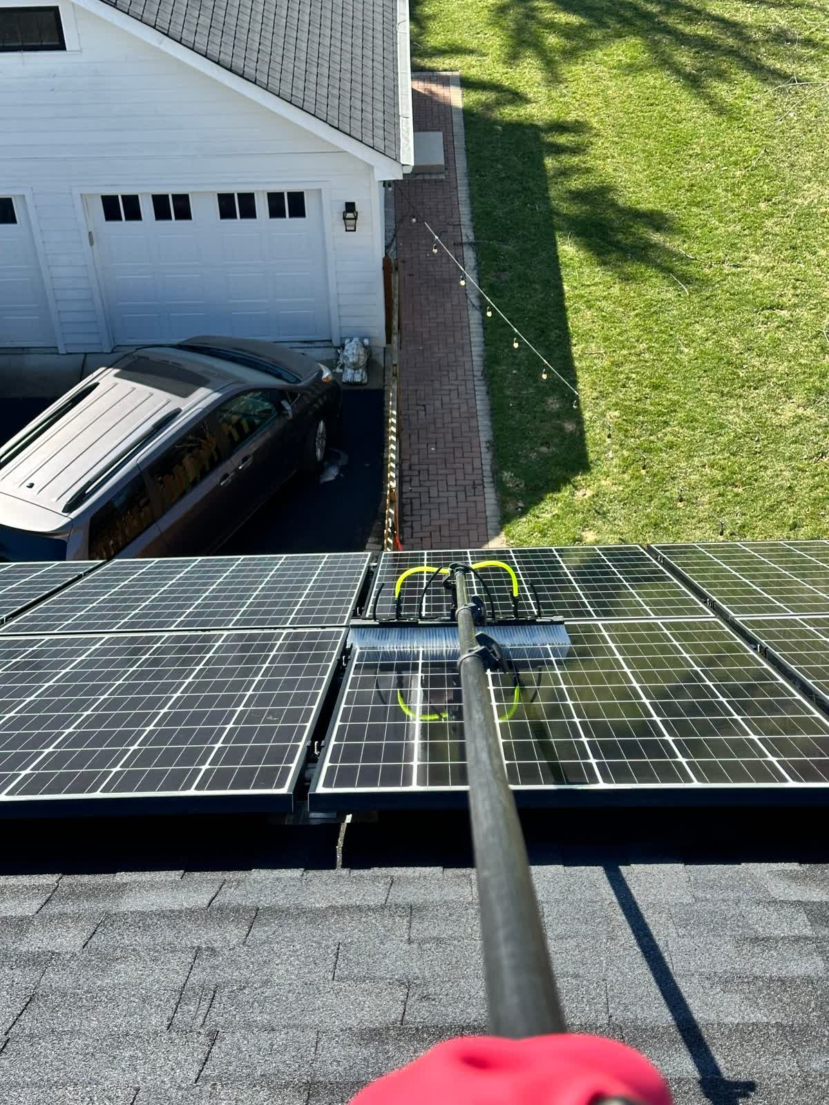 Water-fed pole with a soft-bristle brush cleaning a rooftop solar array at a Glen Ellyn, IL home — cleaned panels visibly glossier than the still-dusty ones beside them